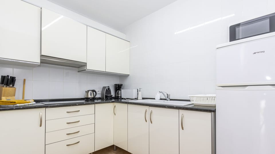 Bright fully equipped kitchen with white cabinets, dark countertop and essential appliances.