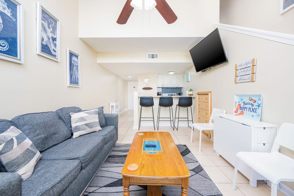 The living area features a cozy gray sofa, a mounted TV, and a stylish kitchen bar, perfect for relaxing and entertaining