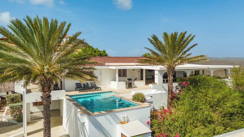 Beautiful pool area surrounded by palm trees and tropical gardens, offering stunning views and direct access to the villa’s main living spaces.