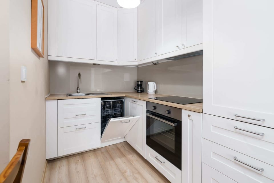 A compact kitchen with white cabinetry, integrated appliances, and a wooden countertop.
