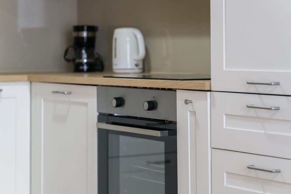 A close-up of a stovetop, white cabinets, and a kettle sitting on the counter.
