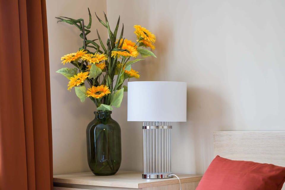 A close-up of a bedside table adorned with a vase of yellow flowers and a modern lamp.
