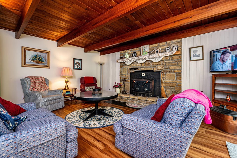 Two wooden spindle beds with floral quilts face a stone accent wall beneath a vaulted wood ceiling with exposed beams.