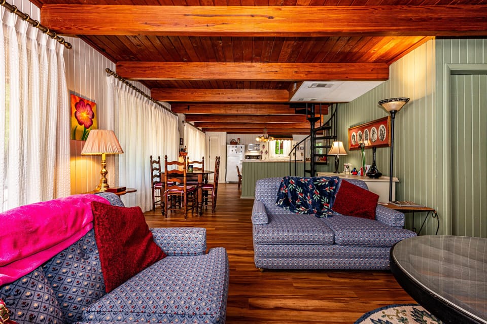 Living room with patterned blue sofas, floral throw, wooden ceiling beams, and a spiral staircase to the loft.