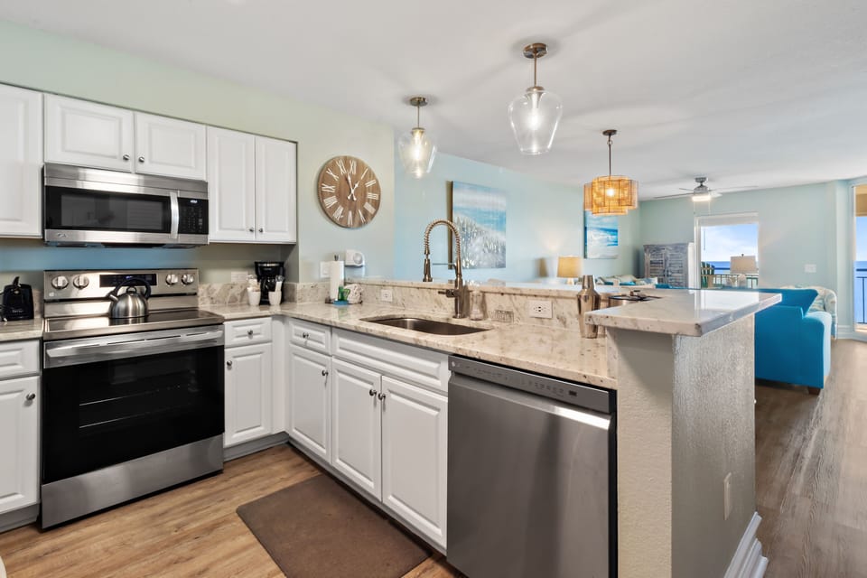 Your fully equipped kitchen awaits with stainless appliances, granite counters, and bright coastal design—perfect for preparing meals.