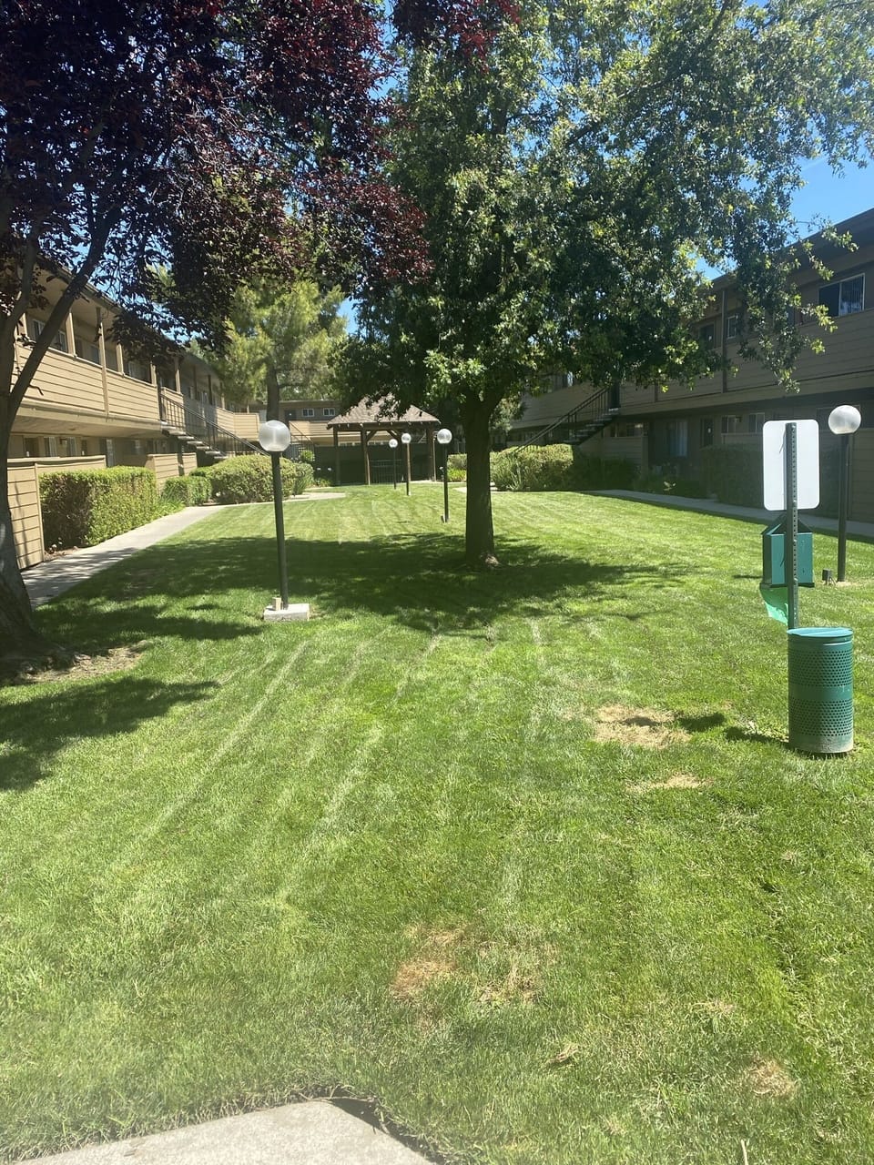 Walkway facing office. Grass, doggy bags and trash can. Gazebo+bbq in distance.