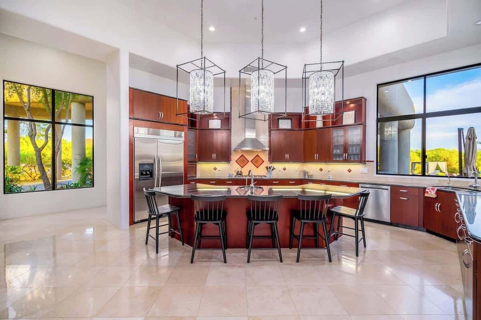 Gather with your group at the spacious island under elegant pendant lighting. Rich wood cabinets and stainless steel appliances surround you, while natural light pours through expansive windows framing desert views.