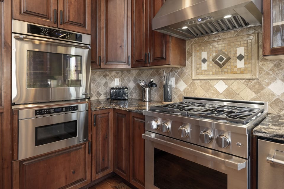 A modern chefs kitchen with stainless steel appliances, including a double oven, gas stove, and range hood