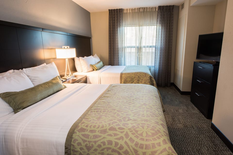 Bedroom with two queen beds, bedside lamp, TV, and curtains.