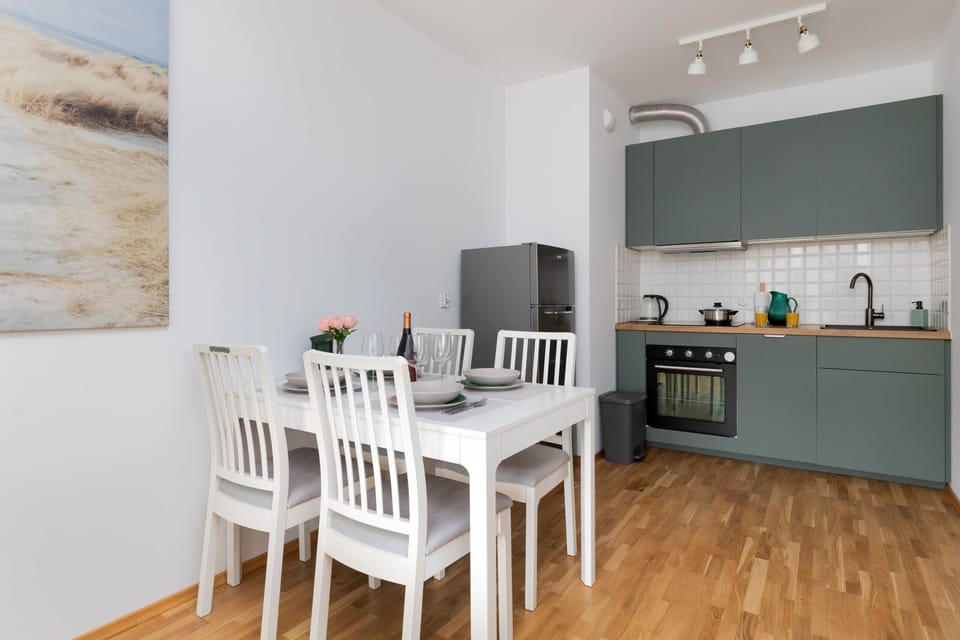 A bright dining space with a white table and chairs beside a modern kitchen equipped with light green cabinets.