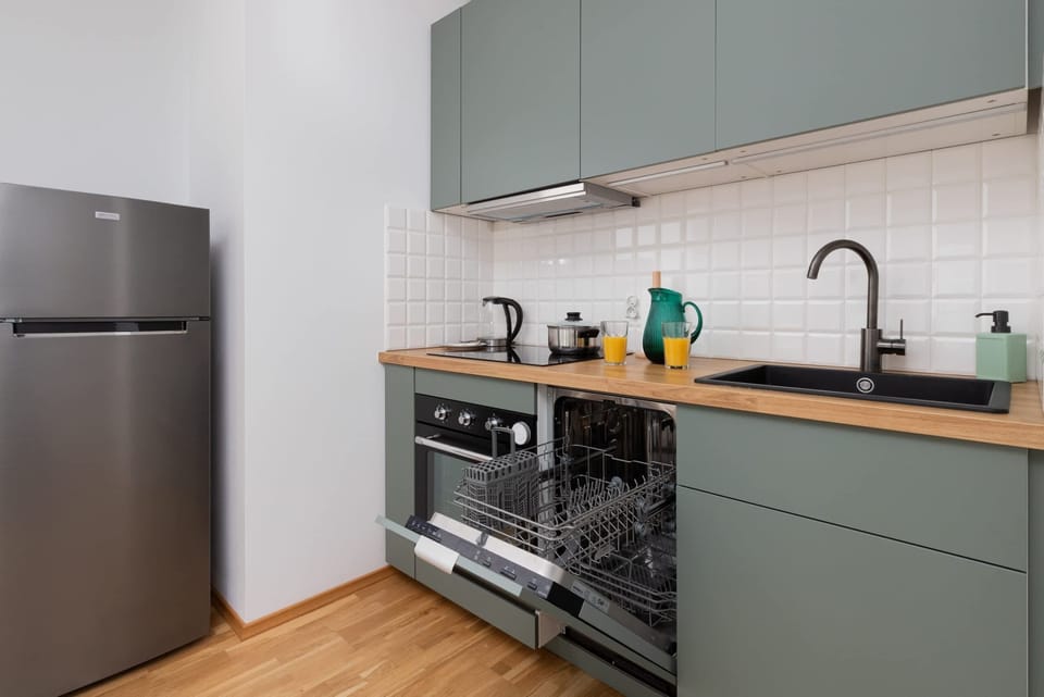 A compact kitchen featuring green cabinets, a stainless steel refrigerator, and an oven, styled with a clean and modern look.