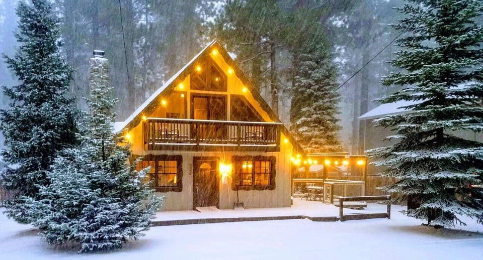 Charming A-frame cabin glows warmly amid snow-covered evergreens, creating the perfect winter mountain retreat.