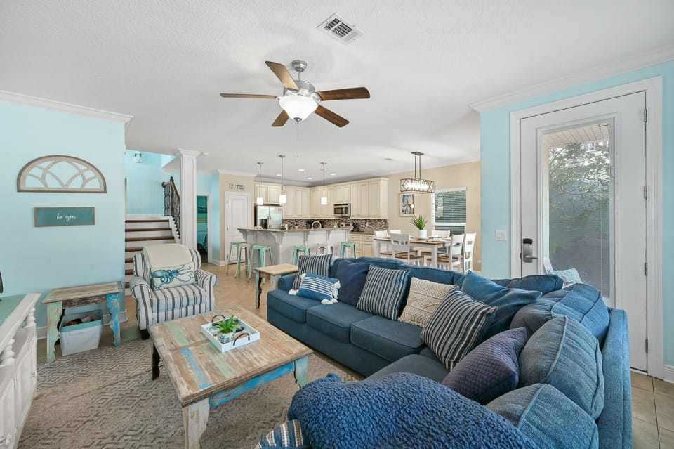 Relax in your spacious living room with plush blue sectional seating, coastal decor, and open kitchen views.