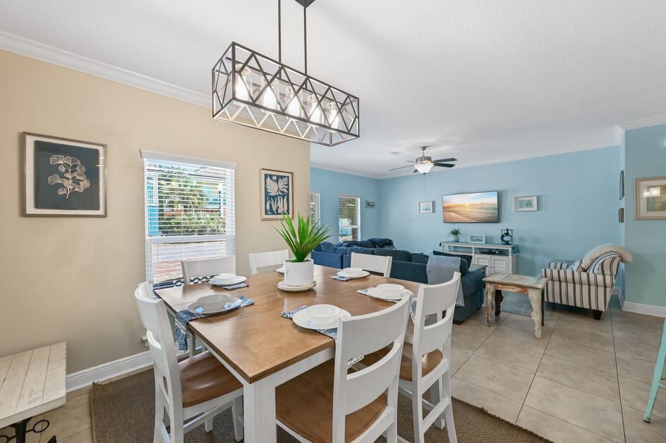 Gather around your elegant dining table beneath the striking geometric chandelier, where coastal blues and warm tones create the perfect atmosphere for memorable meals.