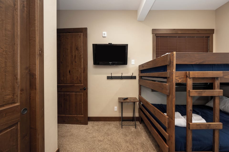 Your cozy bunk room features sturdy wooden beds with navy bedding, wall-mounted TV for entertainment, and rustic touches throughout.