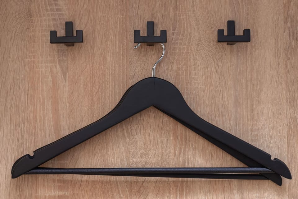 A wooden coat rack with hooks and a black hanger neatly displayed.
