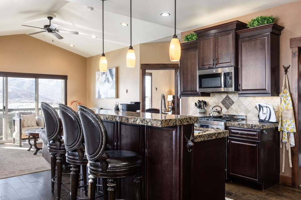 - Kitchen bar with granite counters and tall leather stools  
- Pendant lighting creates a warm and welcoming glow  
- Easy access to living room with open floor plan design