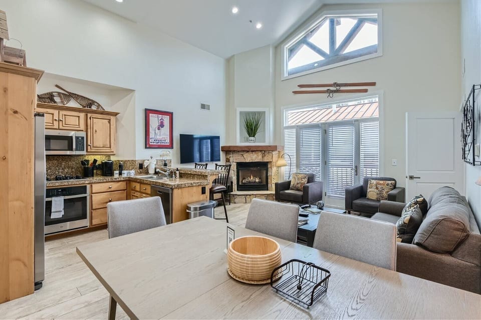 - Open dining and living area with vaulted ceilings and bright light  
- Comfortable seating and stone fireplace for cozy evenings indoors  
- Stylish mountain decor creates a welcoming and homey atmosphere