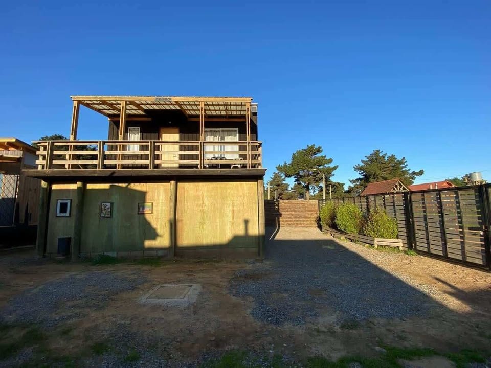 Two-story cabin exterior w/ fenced yard & gravel driveway