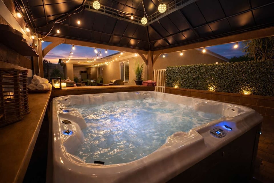 Unwind in the private hot tub at dusk, surrounded by warm lighting and a secluded outdoor lounge designed for relaxation. 