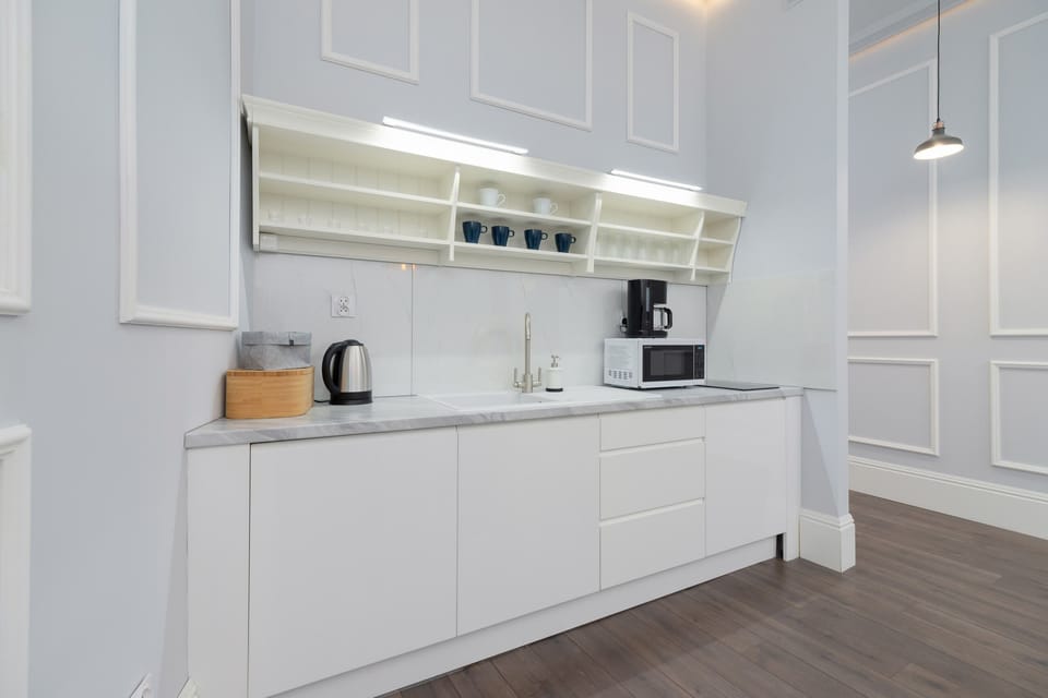 A modern kitchen area with white cabinets, under-cabinet lighting, and a kettle and coffee machine.
