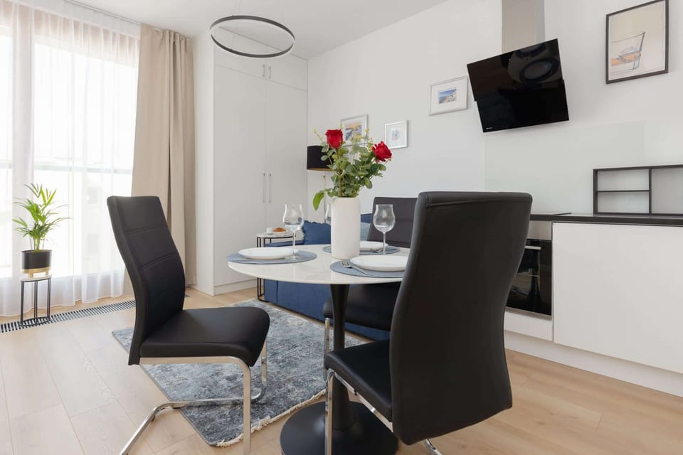 A dining area with a round table, chairs, and a mounted television visible on the wall.
