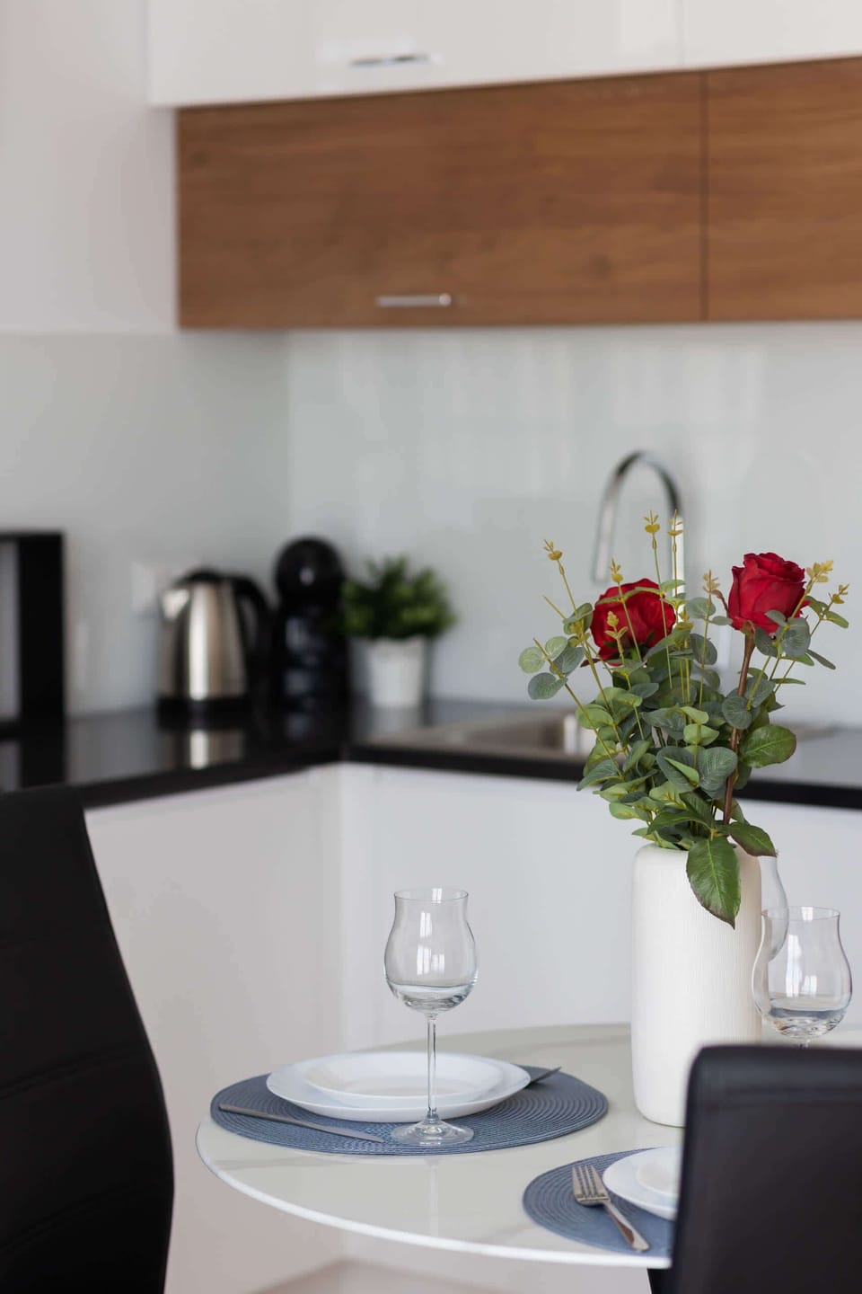 A dining setup with tableware and a vase of fresh flowers, close to the kitchen.
