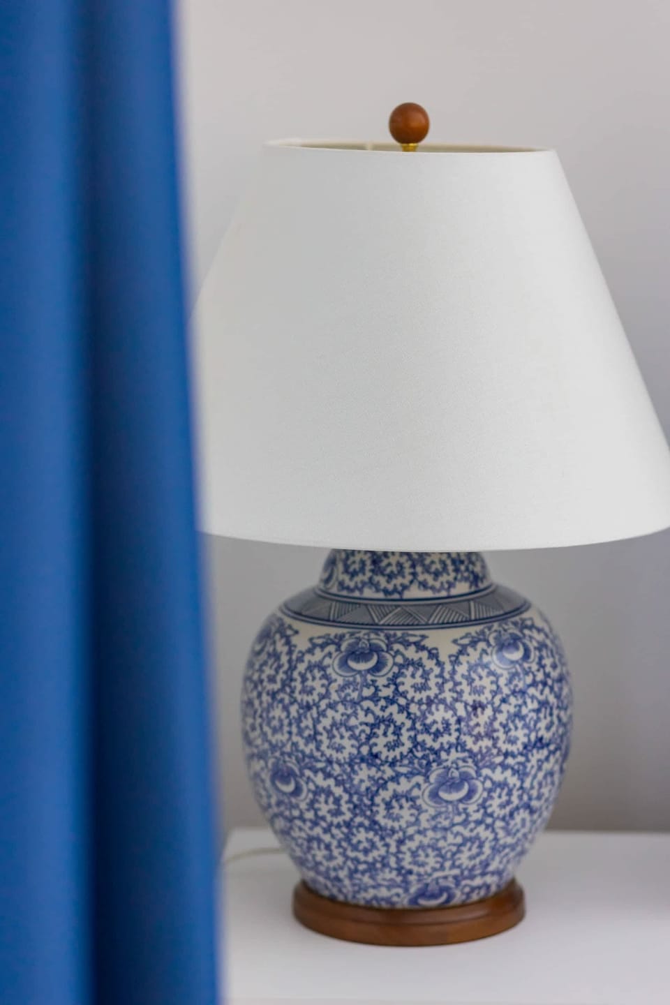 A ceramic table lamp with a classic blue-and-white design, placed next to a blue curtain.
