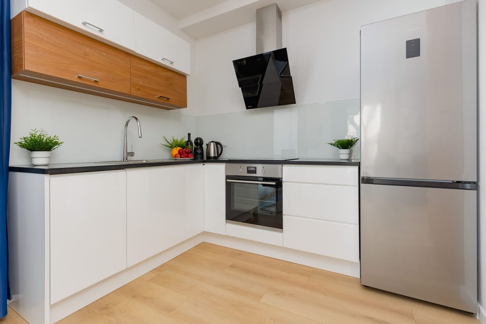 A modern kitchen with white cabinets, wooden accents, and a large silver refrigerator.
