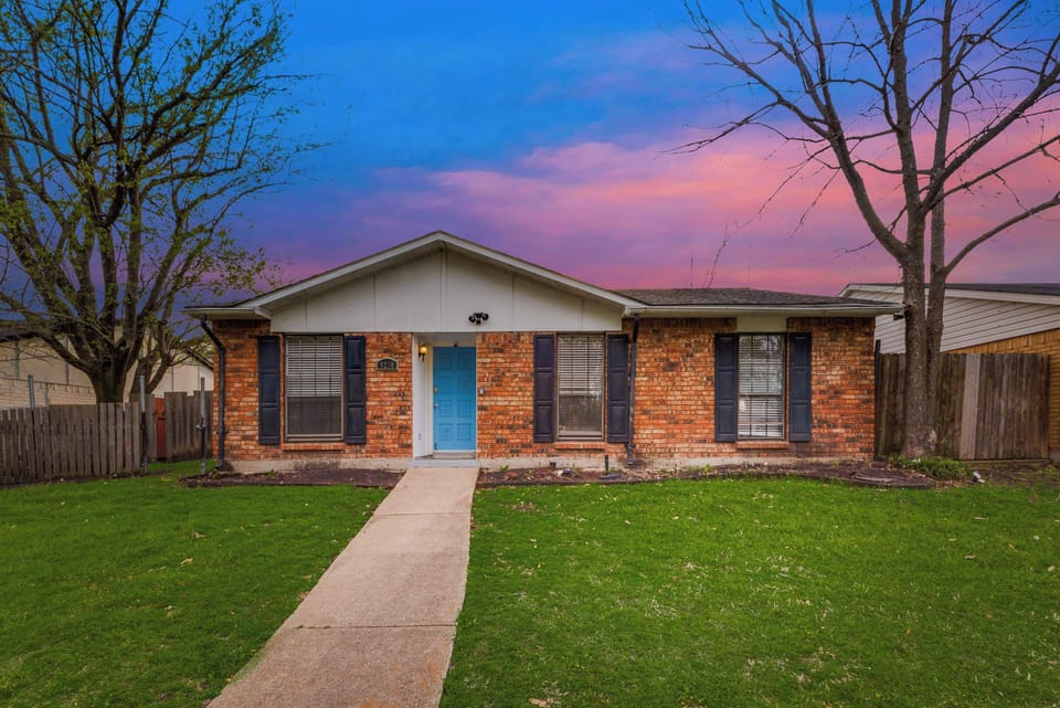 Charming brick home with a pop of color at the front door and a lush green lawn. Perfect welcome for your stay!
