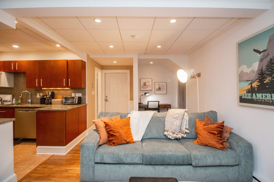 Open-concept space with a cozy sofa, vibrant pillows, modern kitchen, and work nook.