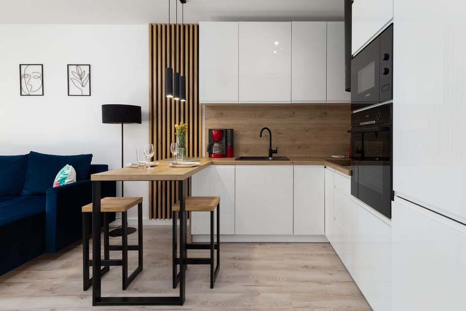 A compact kitchen with modern white cabinets, a black built-in oven, and a small dining area.
