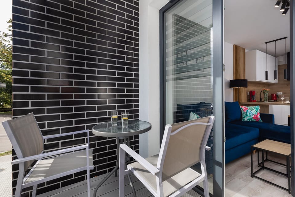 A stylish balcony with black brick walls, a small table, and chairs for outdoor relaxation.
