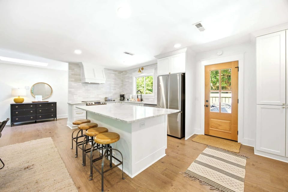 Honey-hued oak floors meet a vast marble island in this airy kitchen, where golden afternoon rays pour through the glass door. Polished steel and industrial stools offer a sleek yet cozy spot to gather for morning coffee and conversation.
