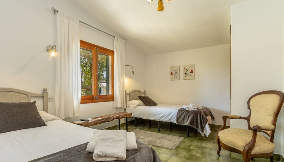 Twin bedroom with natural light, window view and armchair.