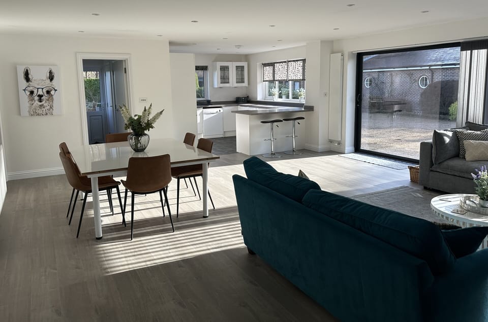 Open plan living area with TV, sofas & dining table, leading to kitchen 