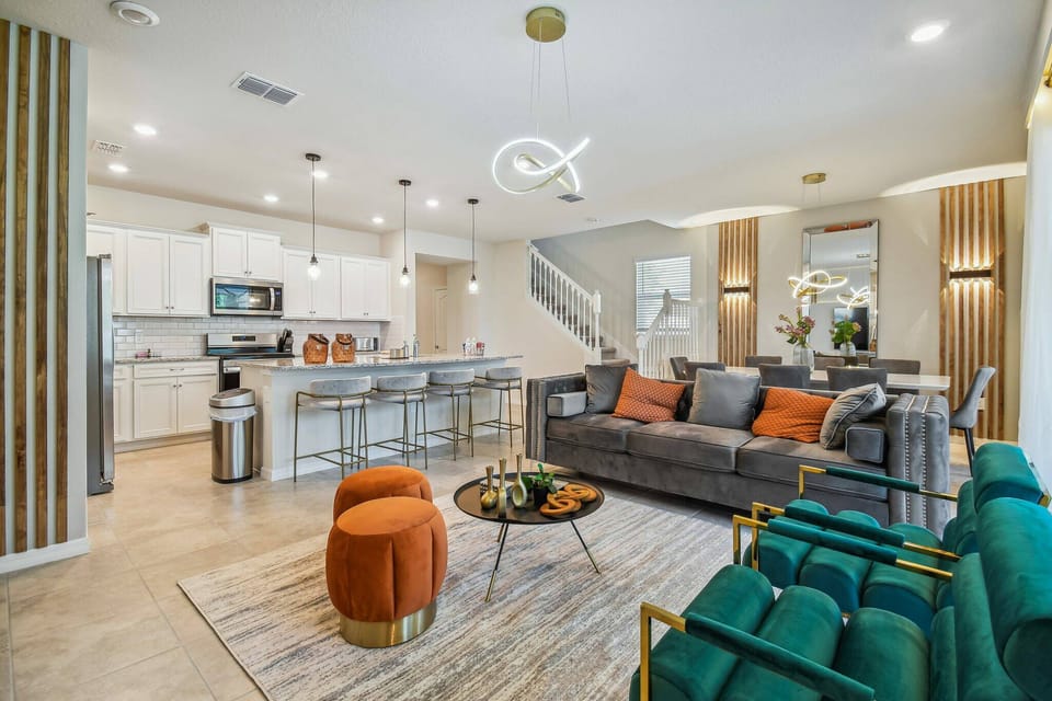 Discover a chic living area with a comfy gray sofa and bright orange pillows. The open layout flows into a sleek kitchen equipped with modern appliances, complemented by warm wooden accents for a touch of sophistication.