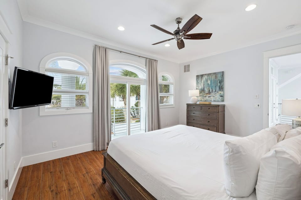Wake up in your elegant master bedroom featuring arched windows overlooking tropical palms, crisp white linens, and private balcony access.