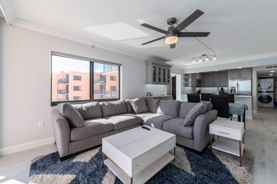 Contemporary gray sectional sofa, plush rug, coastal décor, and a ceiling fan for comfort.