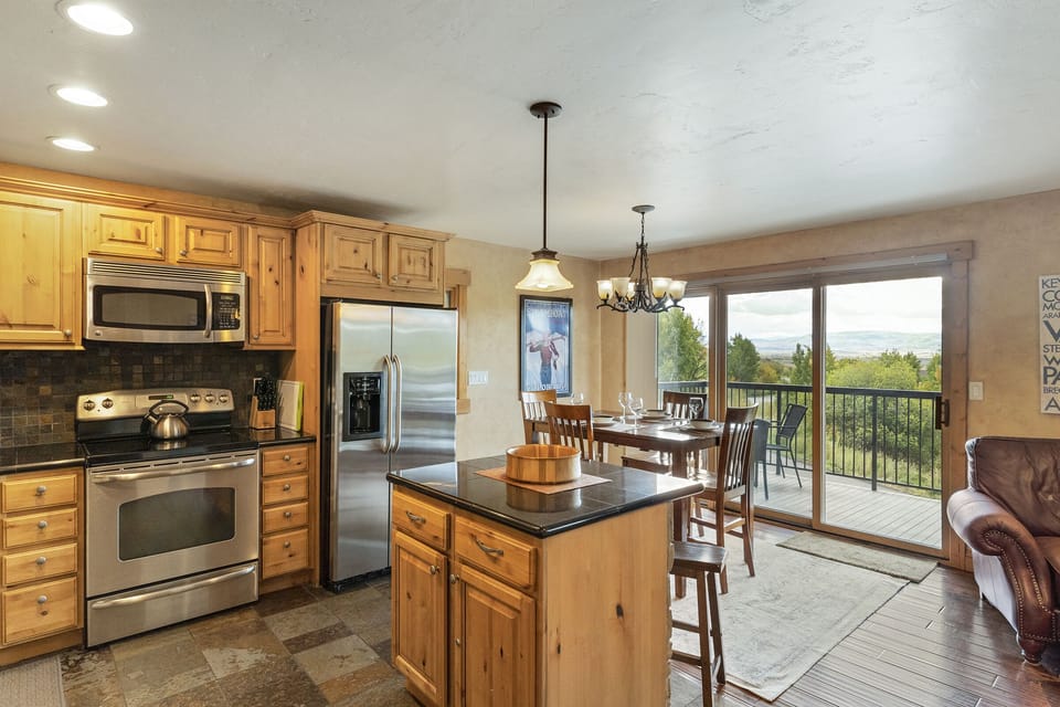 Island bar with granite countertops and seating for two. Dining room behind bar, with large sliding glass door with views of the Yampa Valley.