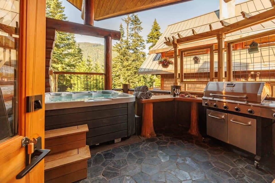 Inviting cabin porch with hot tub and BBQ grill overlooking serene mountain landscape.