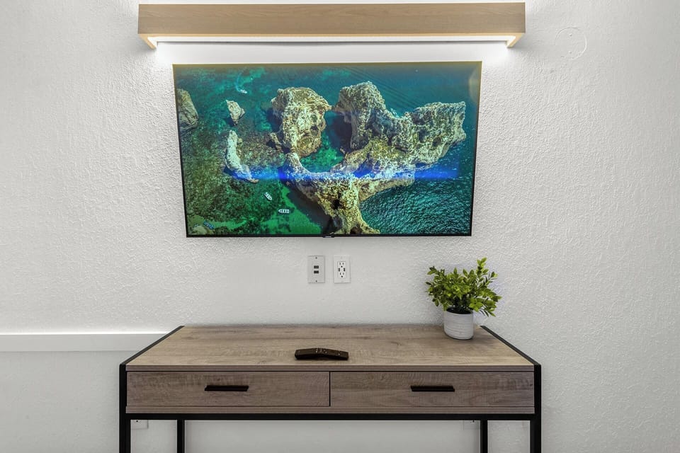 Unwind after a day at the beach with your favorite shows on this sleek flat-screen TV, perfectly set above a modern wood desk—ideal for both entertainment and a touch of productivity during your coastal getaway.