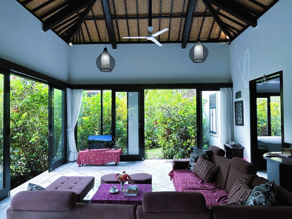 Spacious living room with high ceilings, glass windows, kitchenette & TV.