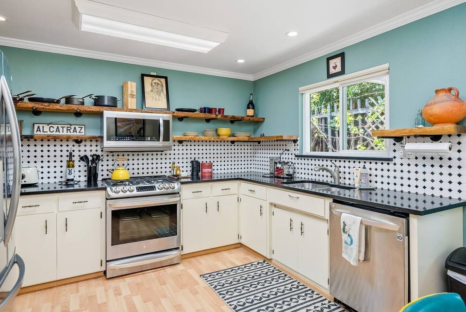 A vibrant chef's kitchen featuring teal walls, live-edge wood shelving, and a striking diamond backsplash. Premium stainless appliances and black countertops offer a stylish, functional workspace for any home cook.