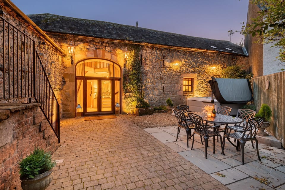 The private patio at night with a hot tub and a dining table and chairs at Rose Walls, Lake District