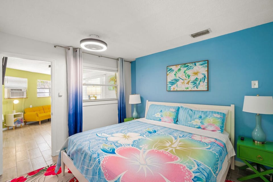 Siesta Key Beach master suite with hibiscus-patterned bedding, a bold blue accent wall, and a floral rug for a bright island escape.