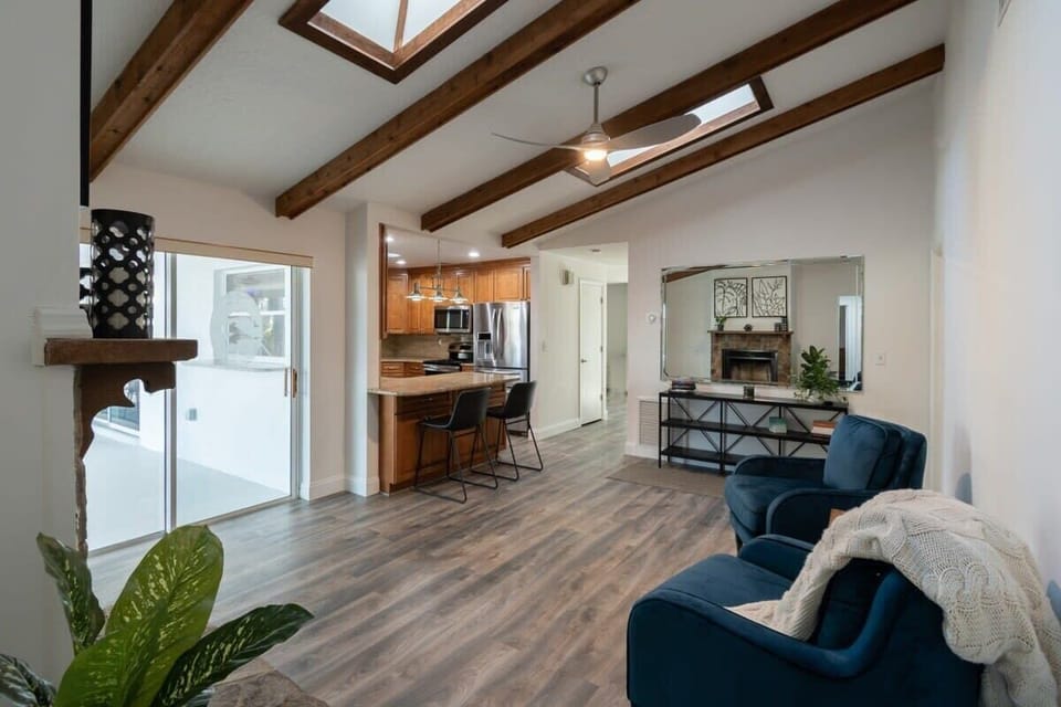 Open living area with vaulted ceilings and skylights connecting to a kitchen with breakfast bar seating.
