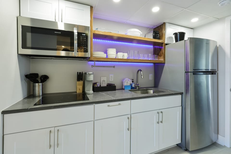 Whip up vacation meals with ease in this sleek, fully stocked kitchenette—complete with stainless steel appliances, open shelving, and a pop of ambient lighting for those cozy, late-night snacks by the beach.
