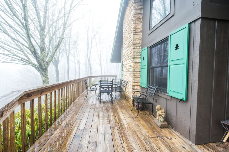 Wooden deck with seating, green shutters, misty forest view, peaceful ambiance.
