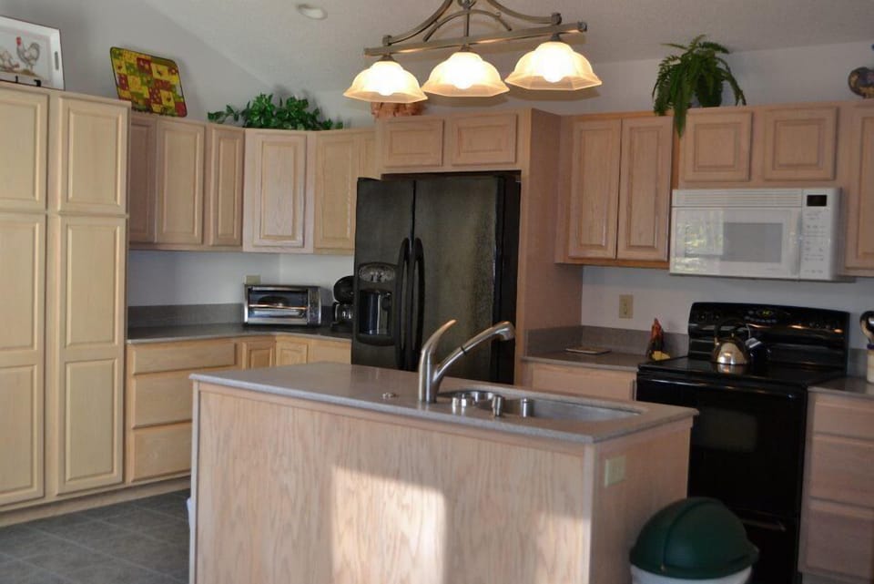 Well-equipped kitchen with light wood cabinets, black appliances, and island.